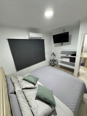 A bedroom with a bed, a TV mounted on the wall, and a built-in shelf unit. - Haven w/ Pool · King Bed · Near Palm Beach #9 (Noord)
