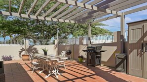 En uteplats med en pergola, ett bord med stolar, en grill och krukväxter.