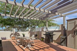 Eine Terrasse im Freien mit einer Pergola, einem Tisch mit Stühlen, einem Grill und Kübelpflanzen.