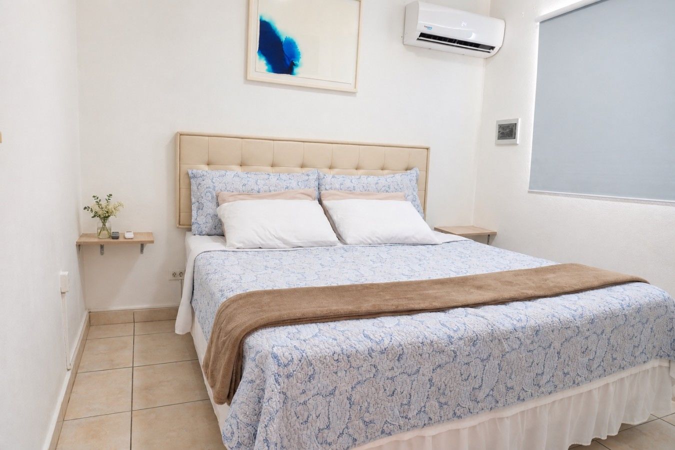 Een slaapkamer met een bed, nachtkastje, wandairconditioner en een raam.