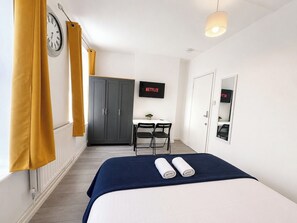 Une chambre d’hôtel avec un lit, un bureau, une chaise, une télévision, une armoire et une horloge au mur.