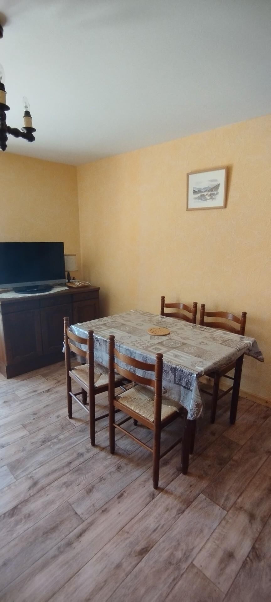 A dining area with a table and chairs, a television on a stand, and a framed picture on the wall.