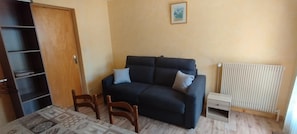 A room with a dark-colored sofa, a wooden cabinet, a small table, and a radiator. - 150m from ski slopes, 1st floor, balcony, parking, 36m², Valloire (Valloire)