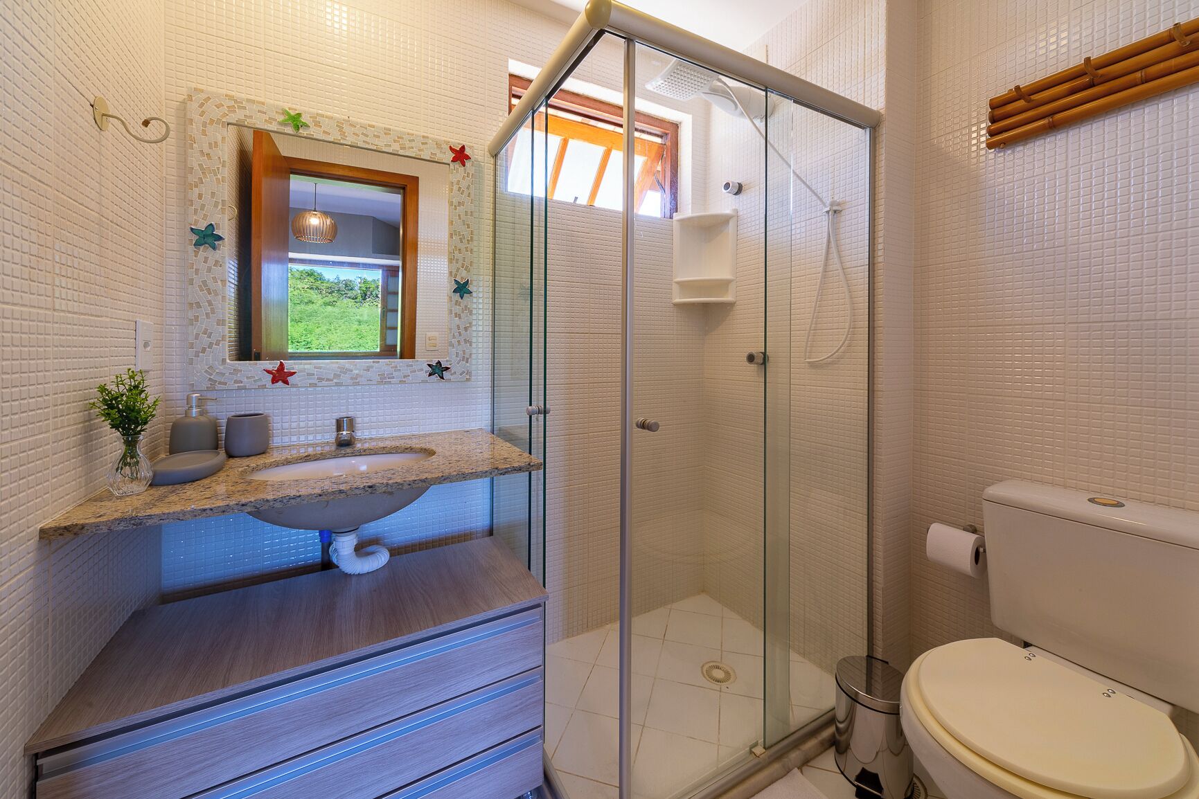 Un bany amb dutxa de vidre, un lavabo amb mirall i un vàter.
