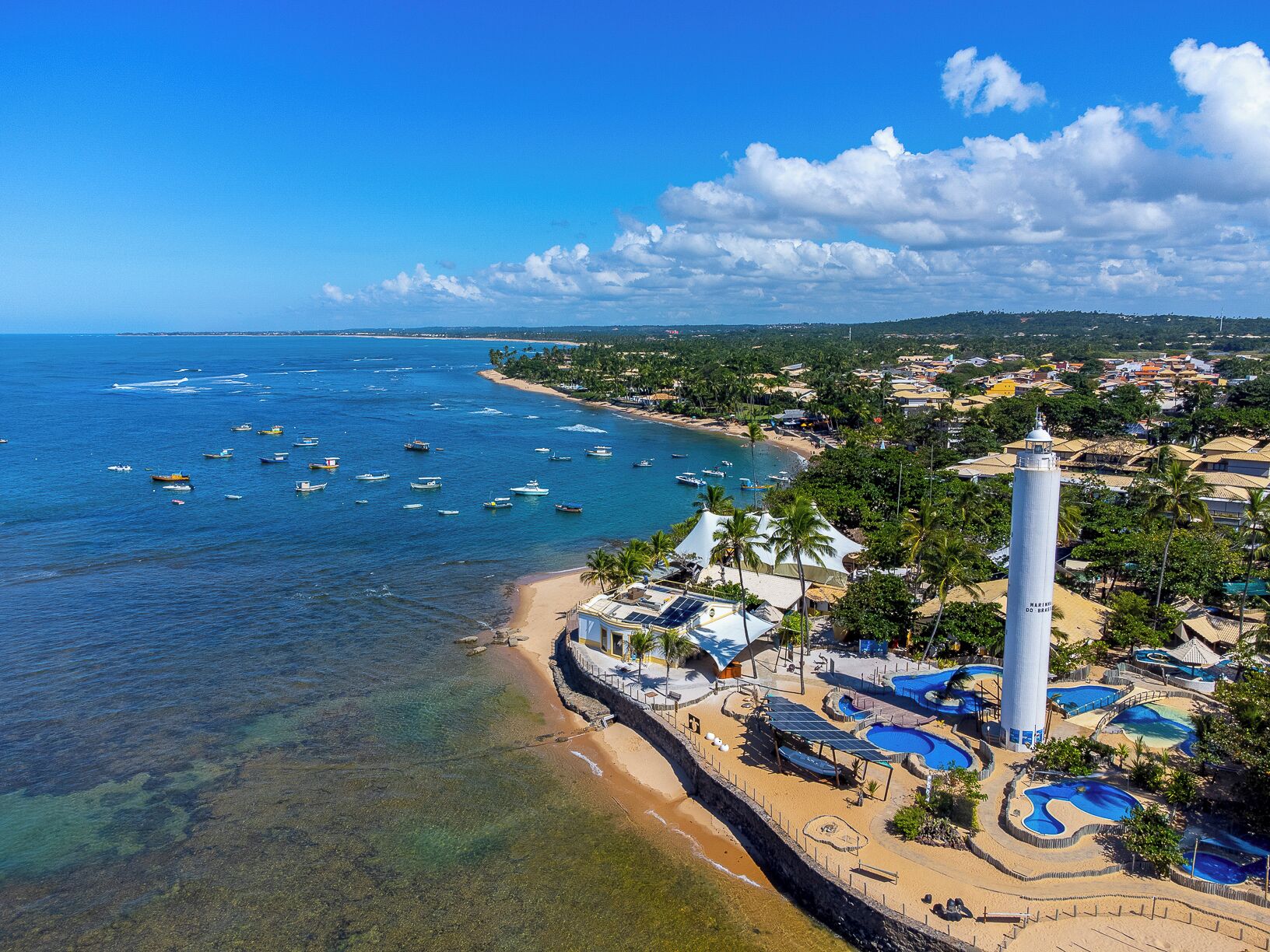 A coastal resort with a lighthouse, clear blue waters, and a sandy beach.