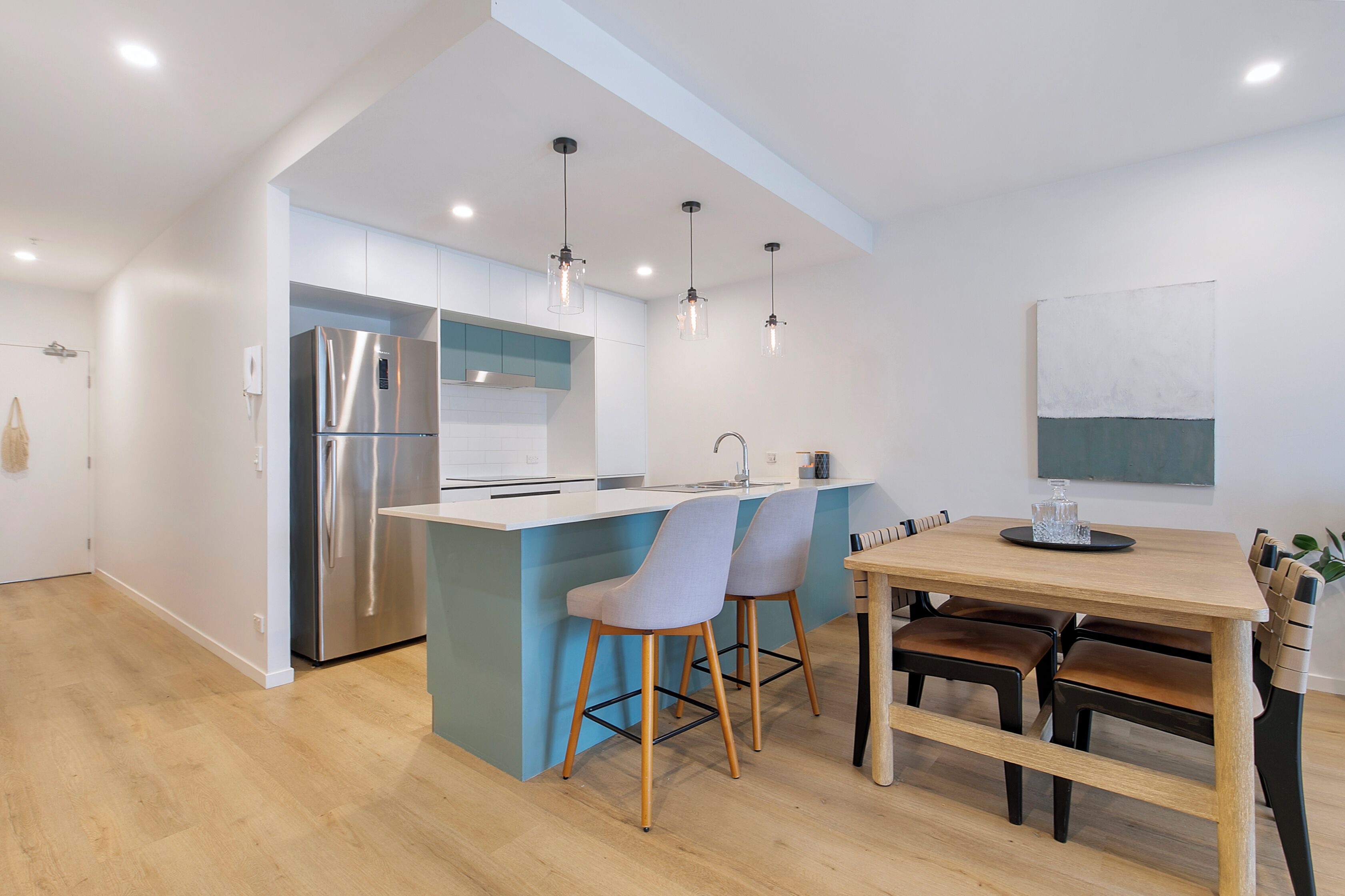 A modern kitchen with a central island, stainless steel appliances, pendant lighting, and a dining area with wooden chairs and a table.