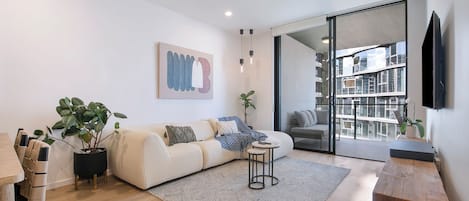 A modern living room with a sofa, a coffee table, a TV, and a large window.
