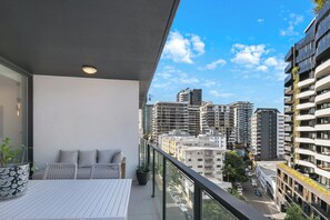 Ein Balkon mit einem weißen Tisch, einem Blumentopf und einer Couch mit Kissen.