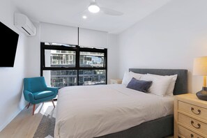 A modern bedroom with a large bed, a blue chair, a nightstand, and a ceiling fan. - Riverstone Perch Urban Comfort near Brisbane River (Newstead)