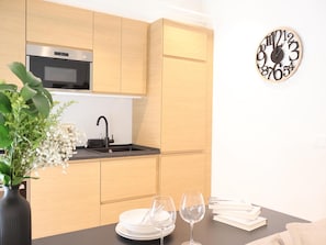 A modern kitchen with wooden cabinets, a built-in microwave, a black faucet, and a wall clock.