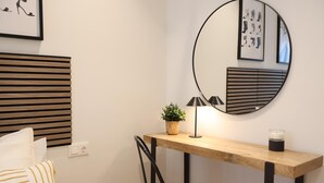 Quarto de hotel com cama, mesa de cabeceira com luminária, espelho e uma obra de arte na parede.