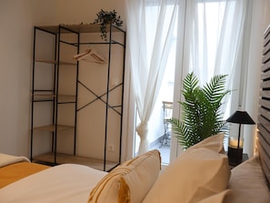 A bedroom with a bed, a wardrobe, a hanging plant, and a bedside table with a lamp.