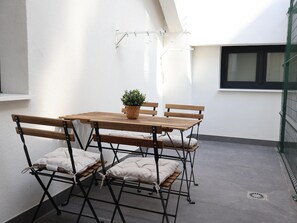 A small outdoor patio with a wooden table and chairs, a potted plant, and a window. - Larrabide Industrial Apartment (Pamplona)