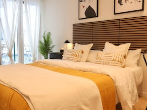A neatly made bed with white bedding and a yellow throw, a bedside lamp, and a framed picture on the wall.