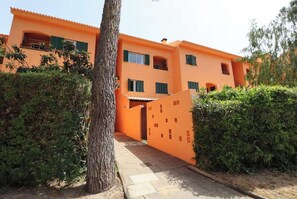 Ein mehrstöckiges Gebäude mit einer leuchtend orangefarbenen Fassade, einem Eingangsbereich mit einem Tor und einem Weg, der zum Eingang führt.