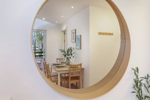 A dining area with a round mirror reflecting a table set for two, wooden chairs, and a vase with greenery. - Aroeira Golf & Wave Retreat (Almada)