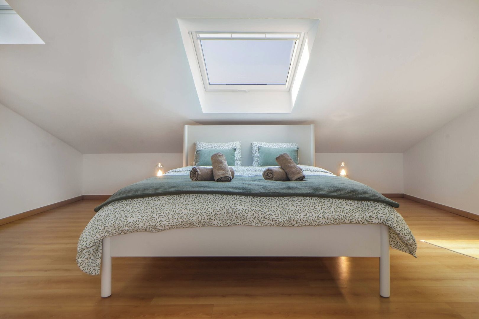 A bedroom with a skylight, a bed with patterned bedding, and a wooden floor.
