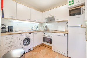 A compact kitchen with a washing machine, oven, microwave, and a coffee machine. - Aroeira Golf & Wave Retreat (Almada)