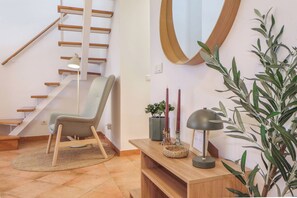 Ein modernes Interieur mit einer Holztreppe, einem grauen Polsterstuhl, einem Holzkonsolentisch mit Dekoration und einem Topfpflanzen.