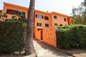 A multi-story building with a bright orange facade, a central entrance, and surrounding greenery. - Aroeira Golf & Wave Retreat (Almada)