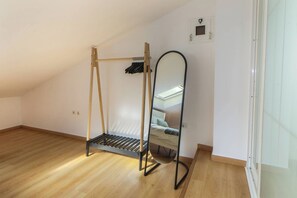 Ein Zimmer mit schrägverdeckter Decke, Holzboden, einem Bett mit Kopfteil und einem Spiegel an der Wand.