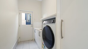Pesuhuone, jossa on pesukone, pieni ikkuna ja ovi, joka johtaa toiseen huoneeseen.