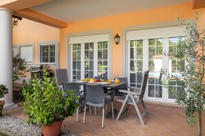 An outdoor patio with a table set for breakfast, surrounded by chairs, and a grill in the background. - Destino Praia D'El Rei - Shared Pool (Óbidos)
