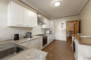 A modern kitchen with white cabinets, a gas stove, a microwave, and a stainless steel sink. - Destino Praia D'El Rei - Shared Pool (Óbidos)