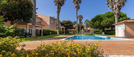 A pool area with a clear sky, surrounded by palm trees and a building with a tiled roof.