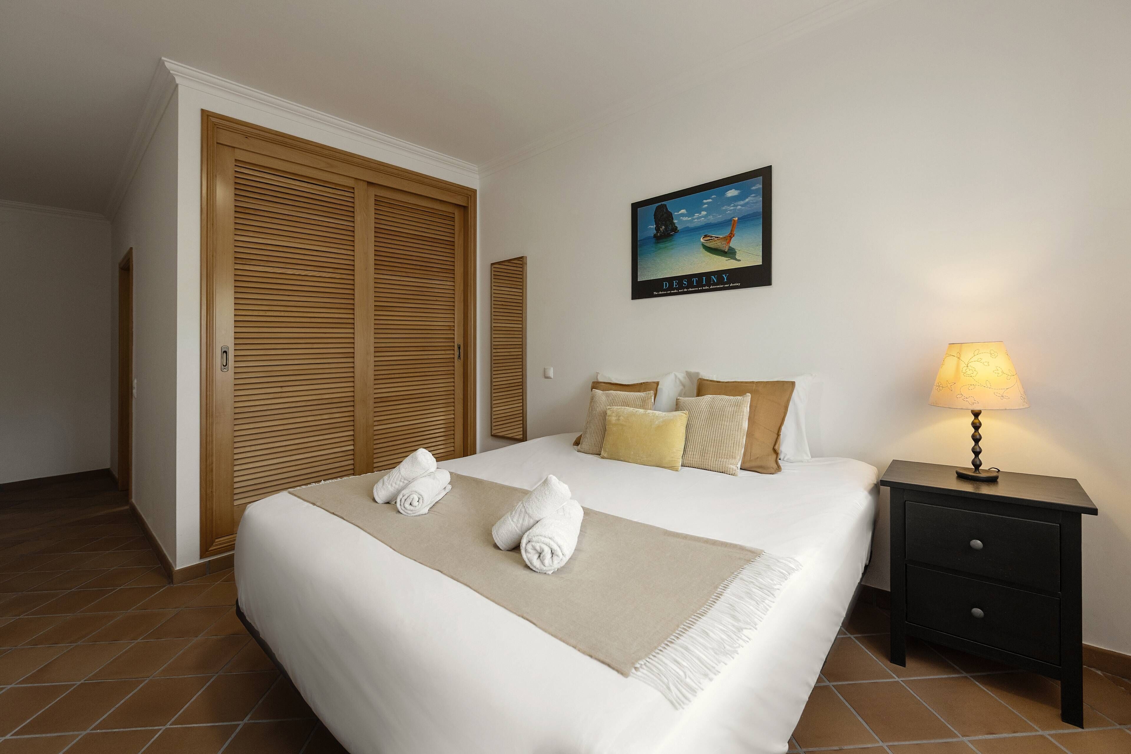 A hotel room with a bed, a nightstand, a lamp, a painting, and a wardrobe.