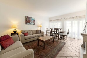 A living room with a sofa, a coffee table, a dining table with chairs, and a painting on the wall. - Destino Praia D'El Rei - Shared Pool (Óbidos)