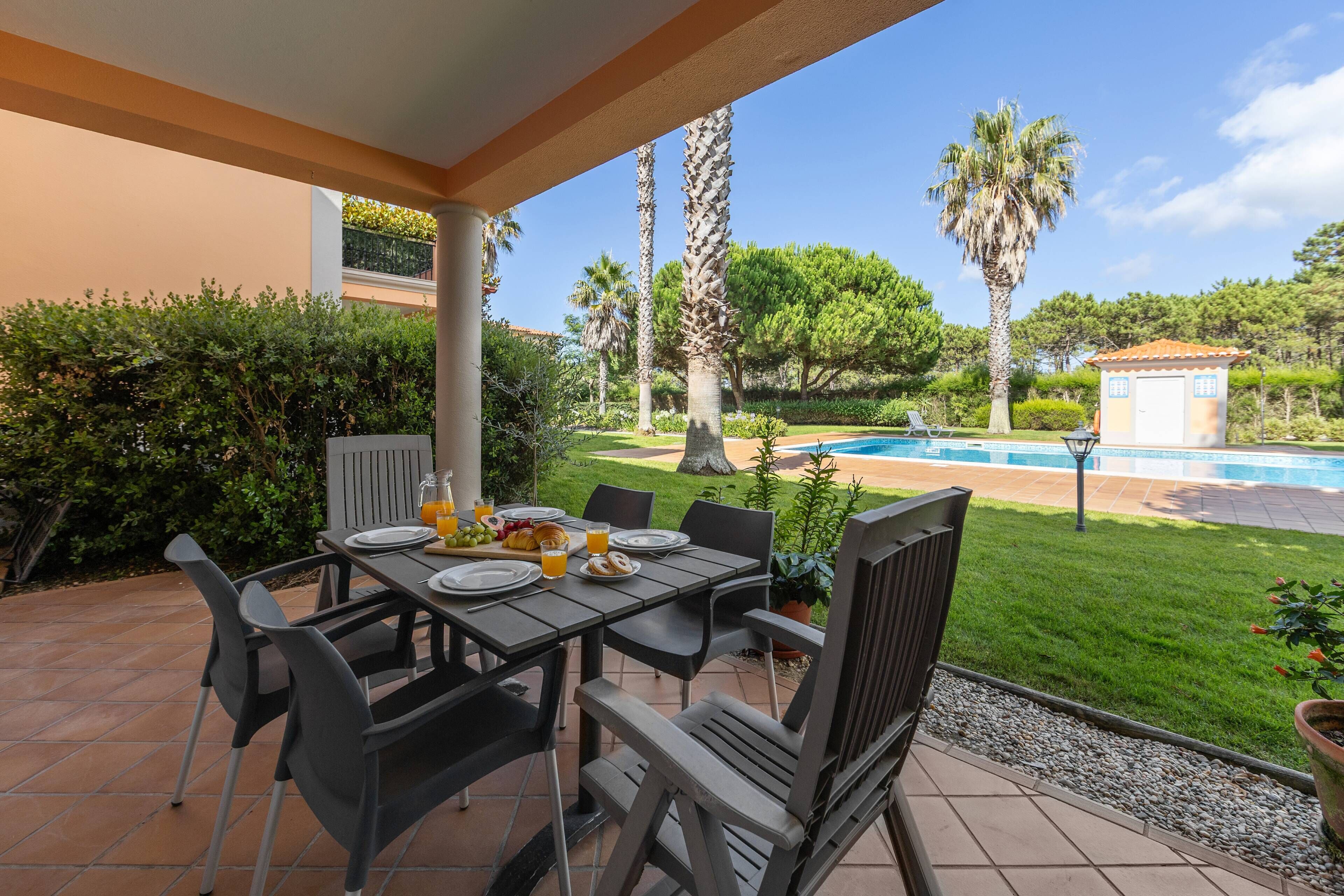 An outdoor patio with a table set for breakfast, a swimming pool, and surrounding greenery.