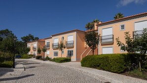 En bostadsgata med flerfamiljshus, kullerstenar och grönska.