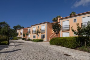 A residential street with multi-story buildings, cobblestone pavement, and greenery. - Destino Praia D'El Rei - Shared Pool (Óbidos)