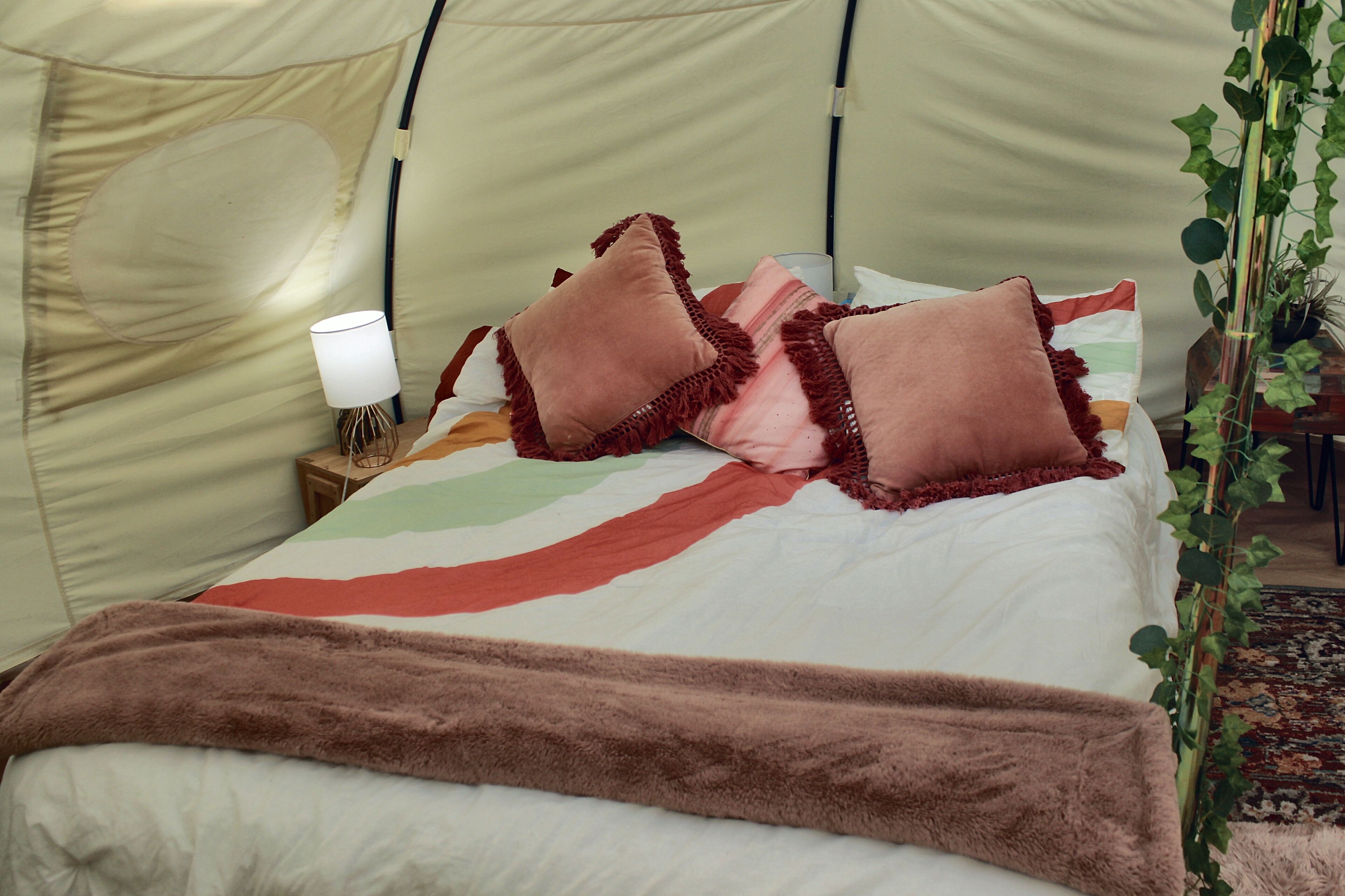Un lit avec une couverture à rayures, un plaid marron et plusieurs coussins.