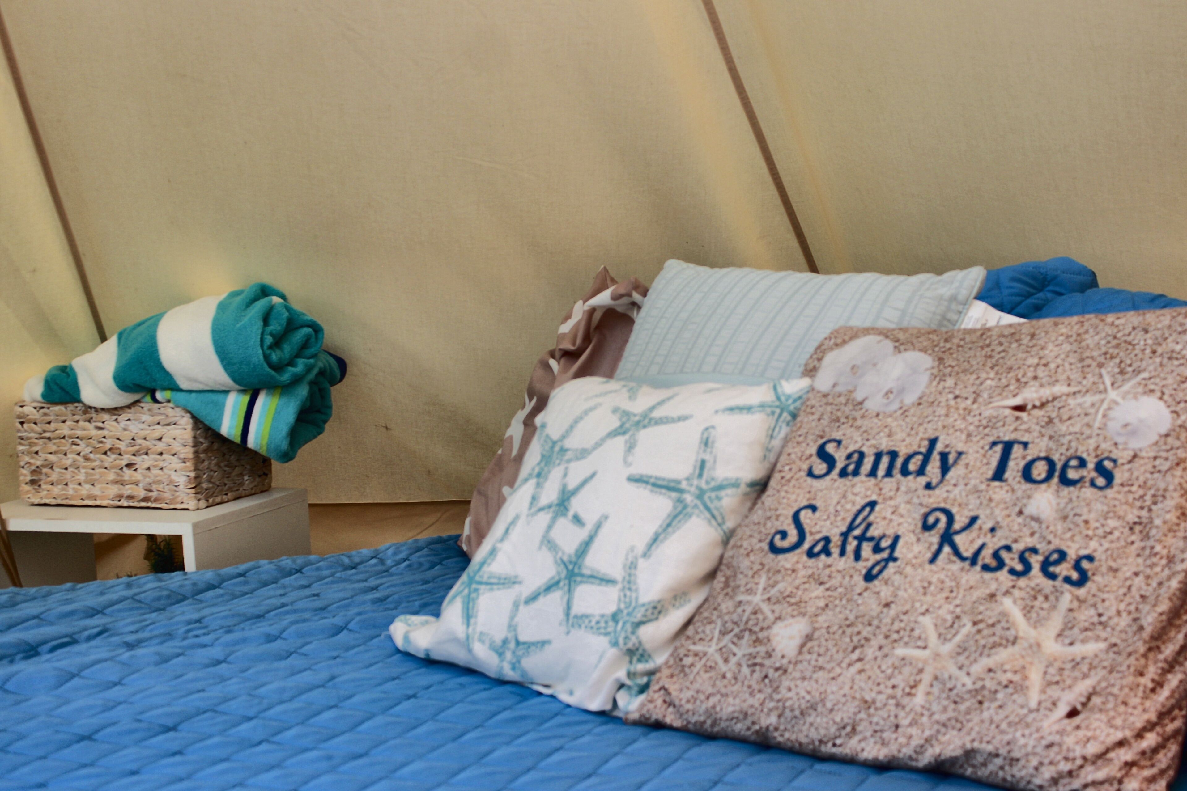 A bed with a blue quilt, a woven basket with a green and white striped towel, and a pillow with a starfish pattern.