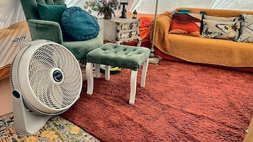 L’intérieur d’une tente, avec un ventilateur, une chaise verte, une petite table avec une lampe et un tapis rouge.