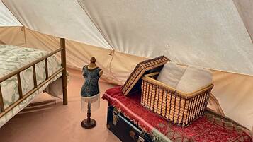 A tent with a bed, a mannequin, and a chest of drawers with a red cloth.