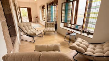 A spacious living area with multiple seating options, large windows with colorful curtains, and a view of the outdoors.