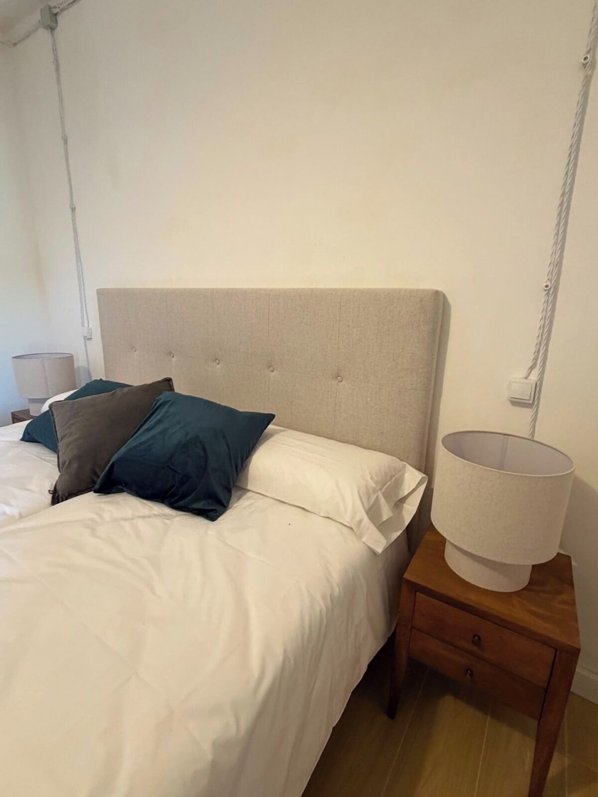 A bed with a headboard, pillows, a bedside table with a lamp, and a wooden nightstand.