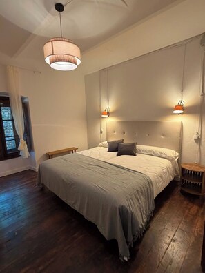 Un dormitorio con una cama grande, dos lámparas de noche, una mesita de noche de madera y una ventana con cortinas.