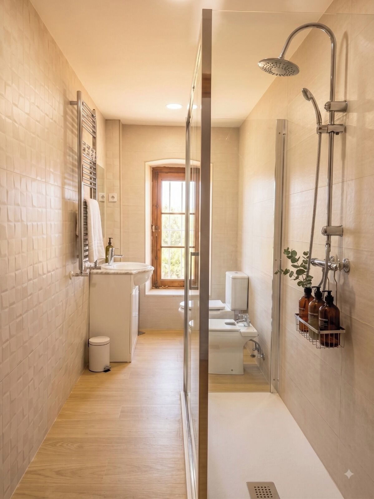 A narrow bathroom with a shower, a toilet, and a sink.