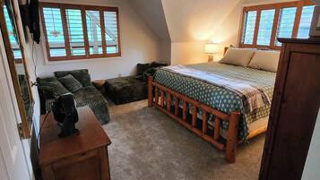 A bedroom with a sloped ceiling, a bed with a wooden headboard, a nightstand, a lamp, and a window with blinds.