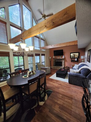 A spacious living area with a dining table, seating, a fireplace, and large windows.