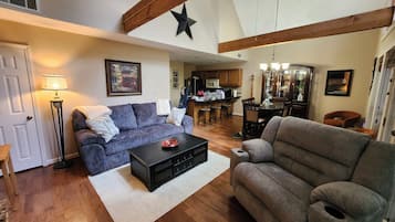 A spacious living room with a fireplace, a dining area, and a kitchen in the background.