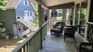 A covered porch with a wooden deck, a staircase, and outdoor furniture.