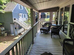 A covered porch with a wooden deck, a staircase, and outdoor furniture.