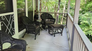 A covered porch with wicker furniture and a view of the surrounding greenery.