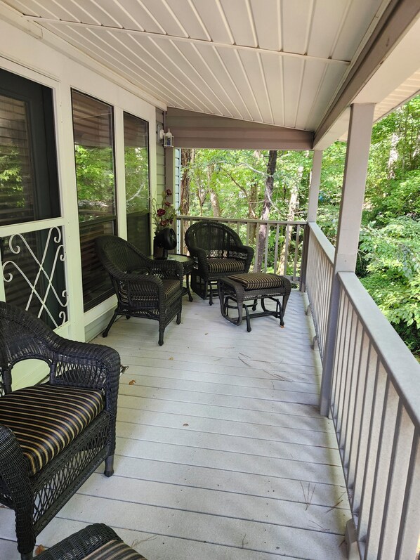 A covered porch with wicker furniture and a view of the surrounding greenery.