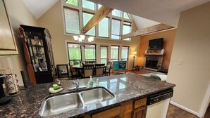 A kitchen with a large island, double sinks, wooden cabinets, a stone fireplace, and a dining area with a table and chairs.